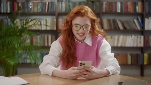 Attractive Student Woman Holding Modern Smartphone Texting Message in Home Office or Library