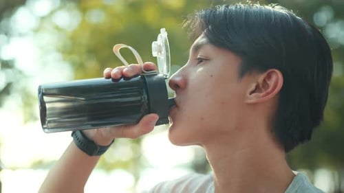 Fitness, Asian man in sportswear drinking water from a bottle during jogging exercise at public park