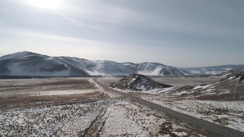 Aerial View on a Road Between the Snowy Hills with a Car Driving on It