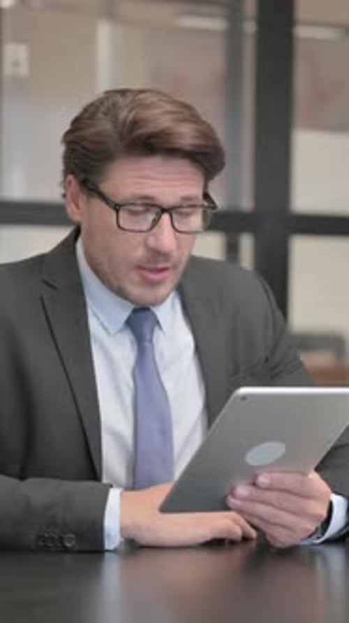 Businessman Doing Video Chat on Tablet in Office, vertical