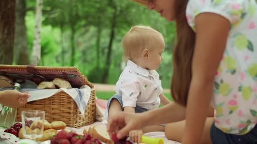 Young Mother with Children Sitting on Blanket in Park. Cheerful Family Having