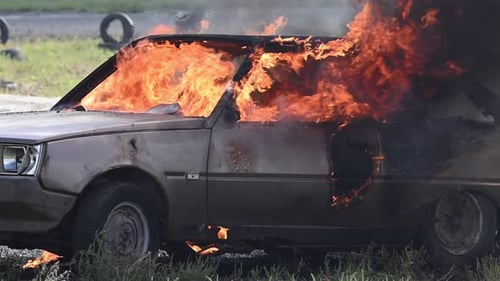 A Car Burns Fiercely in a Field Flames Engulfing the Entire Vehicle Smoke Billows Into the Air As