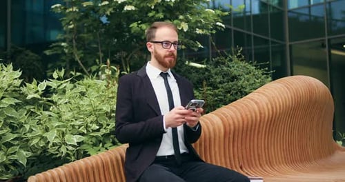 Young businessman analyze data while sitting on bench in business district. Handsome male checking