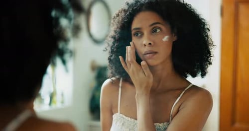 Woman Applying Moisturizer in Bathroom Mirror