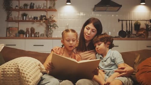 Mother reading book to children on couch indoors