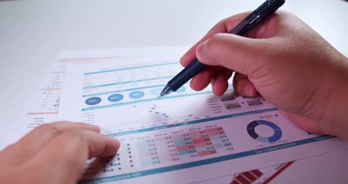 Nahaufnahme der Hände eines Geschäftsmannes mit einem Stift, der am Schreibtisch arbeitet und Dashboard-Grafiken analysiert und c