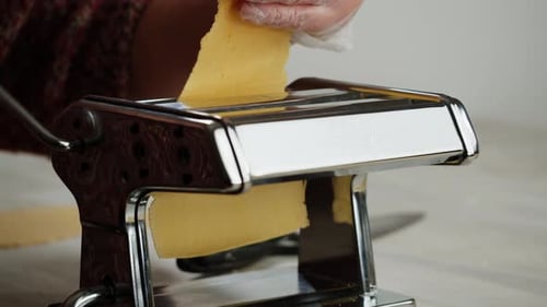 Frau benutzt Nudelmaschine, um frischen Nudelteig in der Küche zuzubereiten und kocht in einem italienischen Restaurant