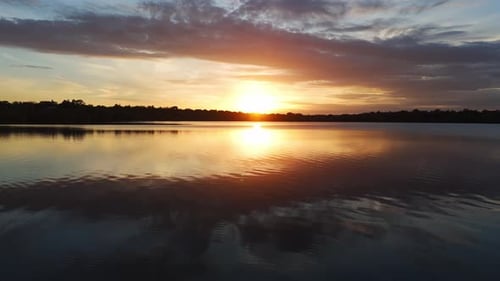 A vibrant sunset reflects off the lake, colors blazing in high contrast as the water ripples gently