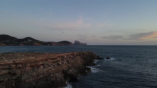 drone view of a cliff above the sea with the incredible background of the ES VEDRÁ island in IBIZA