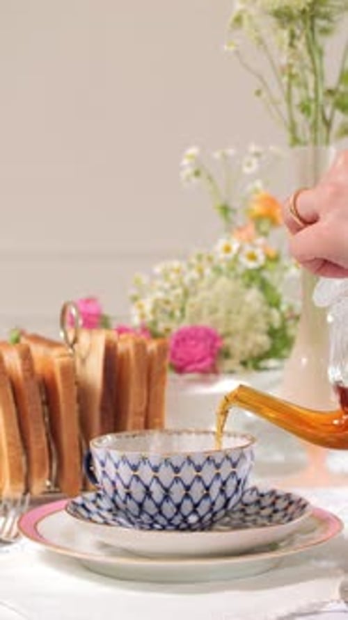 Hand pours Tea into Decorative Teacup