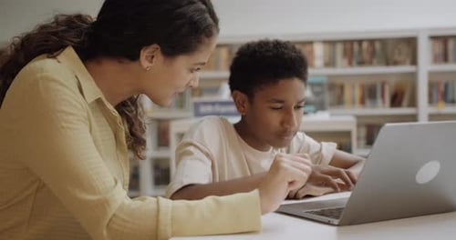 Teacher with School Child in Education Library using Laptop Technology