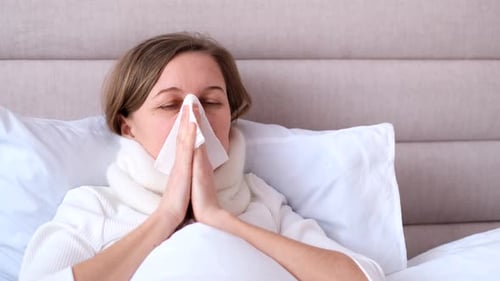 Woman Blowing Nose While Lying in Bed