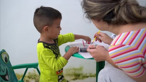 Slow motion of a young latin toddler having painting lessons with a teacher instructor using small b