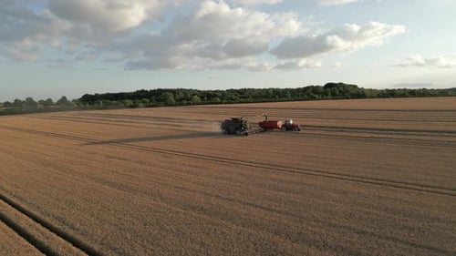 Establishing Drone Shot of Combine Harvester Unloading Grain to Tractor and Trailer at Golden Hour S