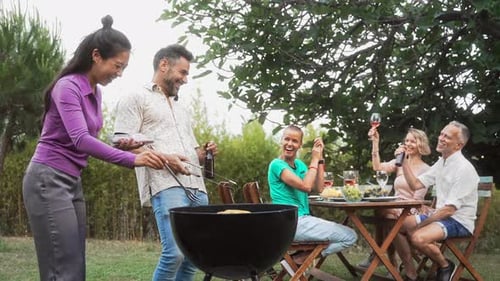 Adult Friends Enjoying Summer BBQ In Garden Party Having Fun Cheering Happy While Cooking