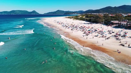 Aerial view of the sea with gentle waves and sandy beach with people relaxing on it