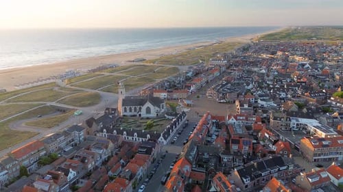 Aerial view of a coastal town with a white church, red roofed homes, and a landscaped courtyard.