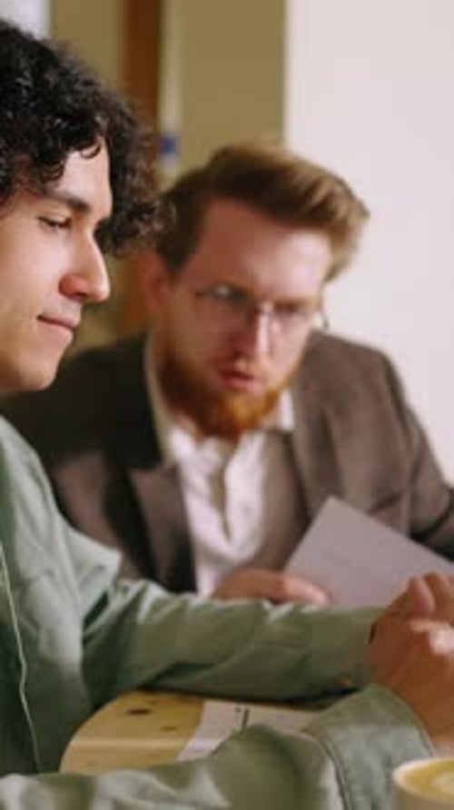 Two Young Colleagues in Casual Meeting Discuss Project Details at Cozy Cafe Table Reviewing