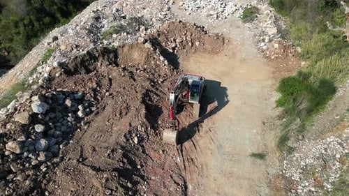 Eine Drohne fliegt über einen Bagger, der in den Bergen neben einem Haufen Erde und Steinen steht