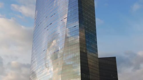 Futuristic and modern skyscraper with glass facade reflecting the sky and clouds, aerial pedestal sh