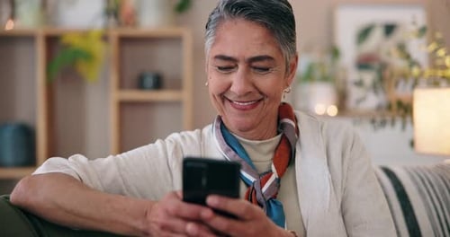 Senior Woman Smiles at Phone in Cozy Home
