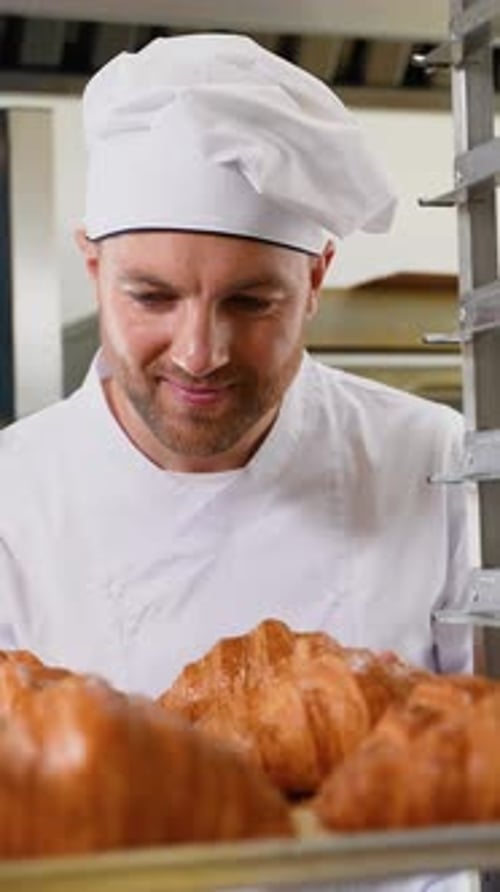 Smiling Baker Holding Tray of Fresh Croissants