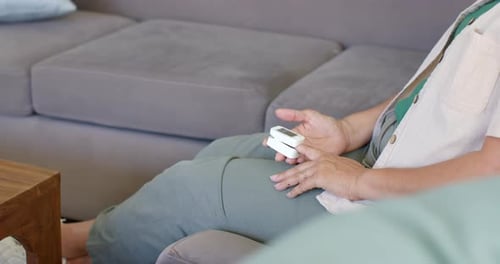 Idoso sentado no sofá, segurando o dispositivo no colo, ajustando e estendendo a mão direita para fora, enfatizando