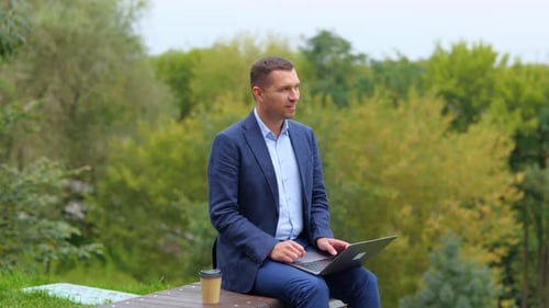 Fröhlicher Geschäftsmann tippt auf Laptop in der Natur, schließt Gerät und lächelt, fühlt sich frei und glücklich