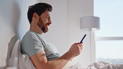 Hombre matutino navegando por teléfono celular en la cama el fin de semana, chico de cerca que busca un teléfono inteligente