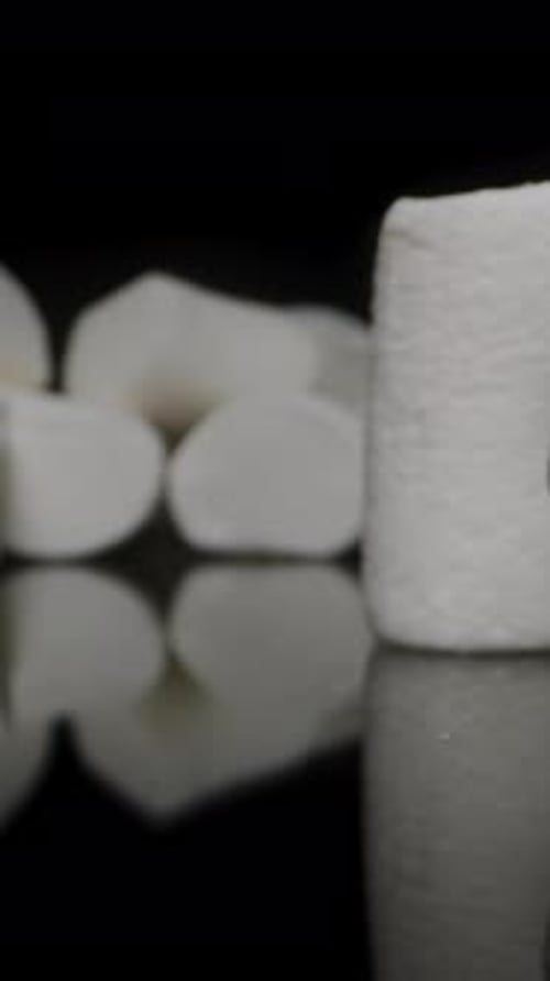 Vertical video. Moving Forward to White Marshmallow on Black Table, Hand Taking Pieces One by One.