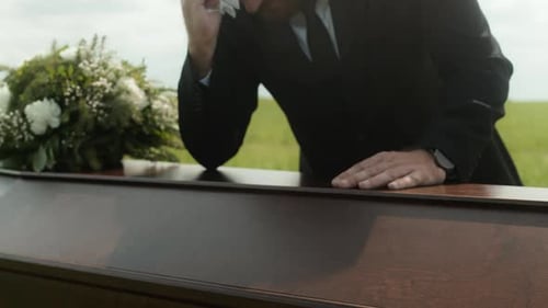 Man Grieving Beside a Coffin in Rural Field