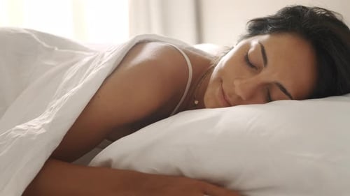 Authentic close up shot of an young brunette woman is sleeping peacefully wrapped in warm duvet bl