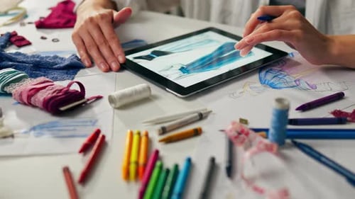 Creative designer illustrating fashion sketches on a digital tablet surrounded by colorful materials