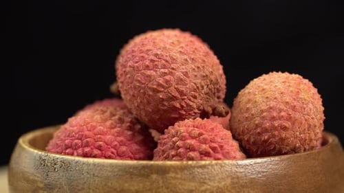 Fresh lychee fruit in shell rotate in wooden bowl in macro on black background. Lychee berries