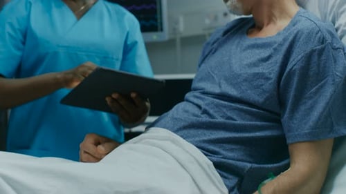 In the Hospital, Senior Patient Lying in the Bed Talking to a Nurse who is Holding Tablet Computer