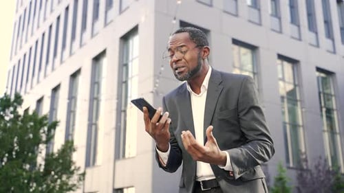 Frustrated Businessman Talking on Phone Outdoors in City