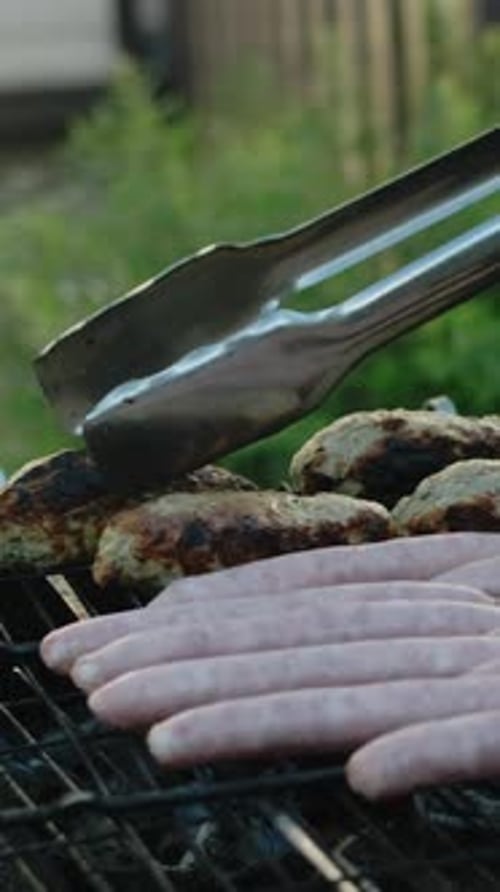 Vertikales Video-Barbecue-Konzept: Hand dreht gegrilltes Fleisch mit einer Zange um