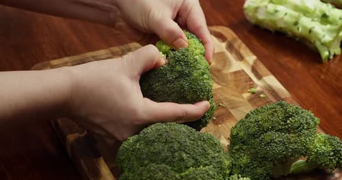 Top View Cook Breaking Fresh Broccoli Into Florets on a Wooden Cutting Board