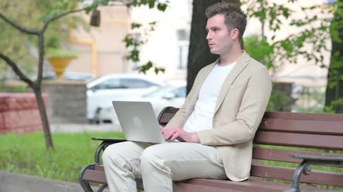 Casual Young Man Thinking and Working on Laptop Outdoor