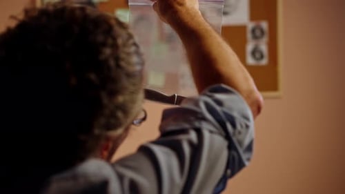 Closeup Detective's Office Middleaged Investigator in Shirt and Tie Sitting Desk Examining Evidence