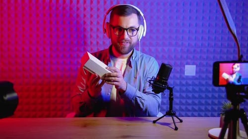 Young Male Technology Blogger Recording Video Blog or Vlog Review of New Smartphone at Home Studio