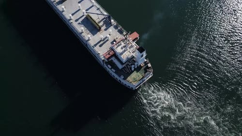 Vue aérienne d'un grand cargo naviguant dans des eaux calmes, la lumière du soleil se reflétant sur la mer