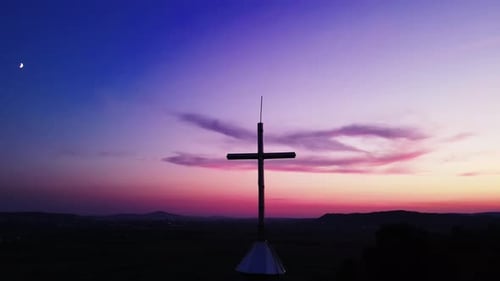 Drone shot of large christian church cross against a pink sky on the setting sun