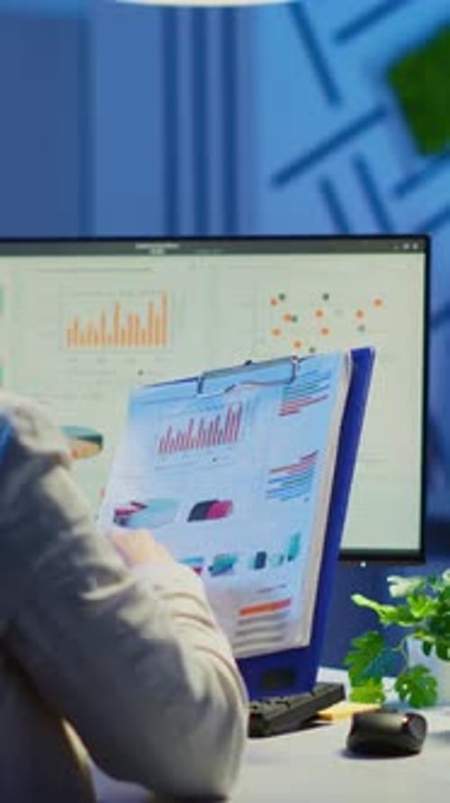 Vertical Video Back View of Manager Analysing Graphics From Clipboard at Midnight