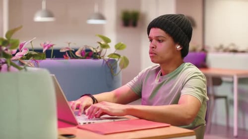 Homme afro-américain en bonnet commençant à travailler dans un café de coworking, tapant sur un ordinateur portable, se penchant en avant