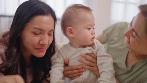 Asian lesbian couple lovingly caring for and raising their baby boy at home.
