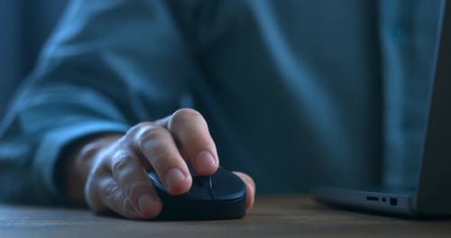Close Up Man's Hand Uses a Computer Mouse While Working on a Laptop in the Evening