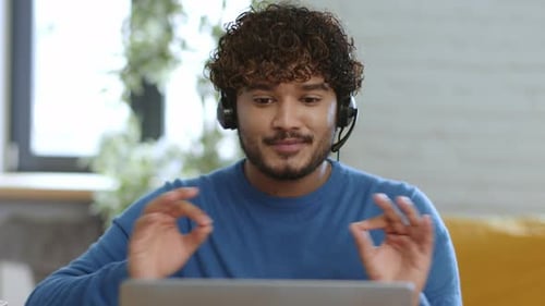 Junger Mann nimmt von zu Hause aus an einem Online-Meeting teil, während er einen Laptop benutzt