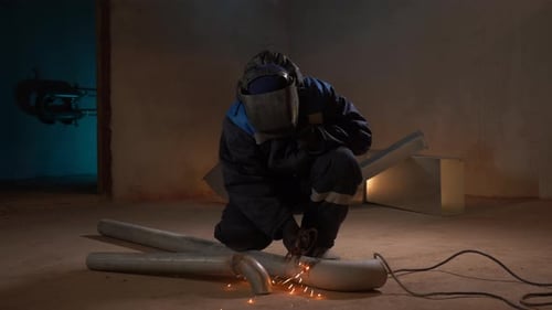 Arbeiter, die Metallrohre mit vielen Funken schweißen, fliegen im Dunkeln in verschiedene Richtungen. Klammer.