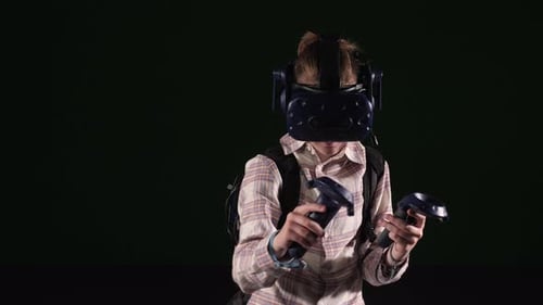 A Teenage Boy in a VR Headset with Joysticks in His Hands is Playing Video Games